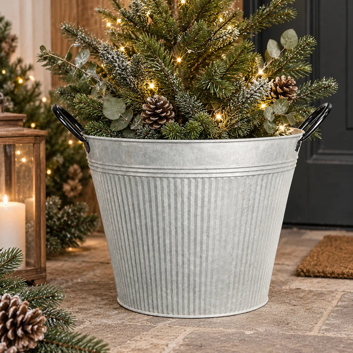 Rustic aged zinc planter pot with fine vertical ribbing and black loop handles filled with evergreen Christmas foliage