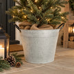 Round ribbed zinc metal planter with black handles holding a small lit fir tree by a country home entrance