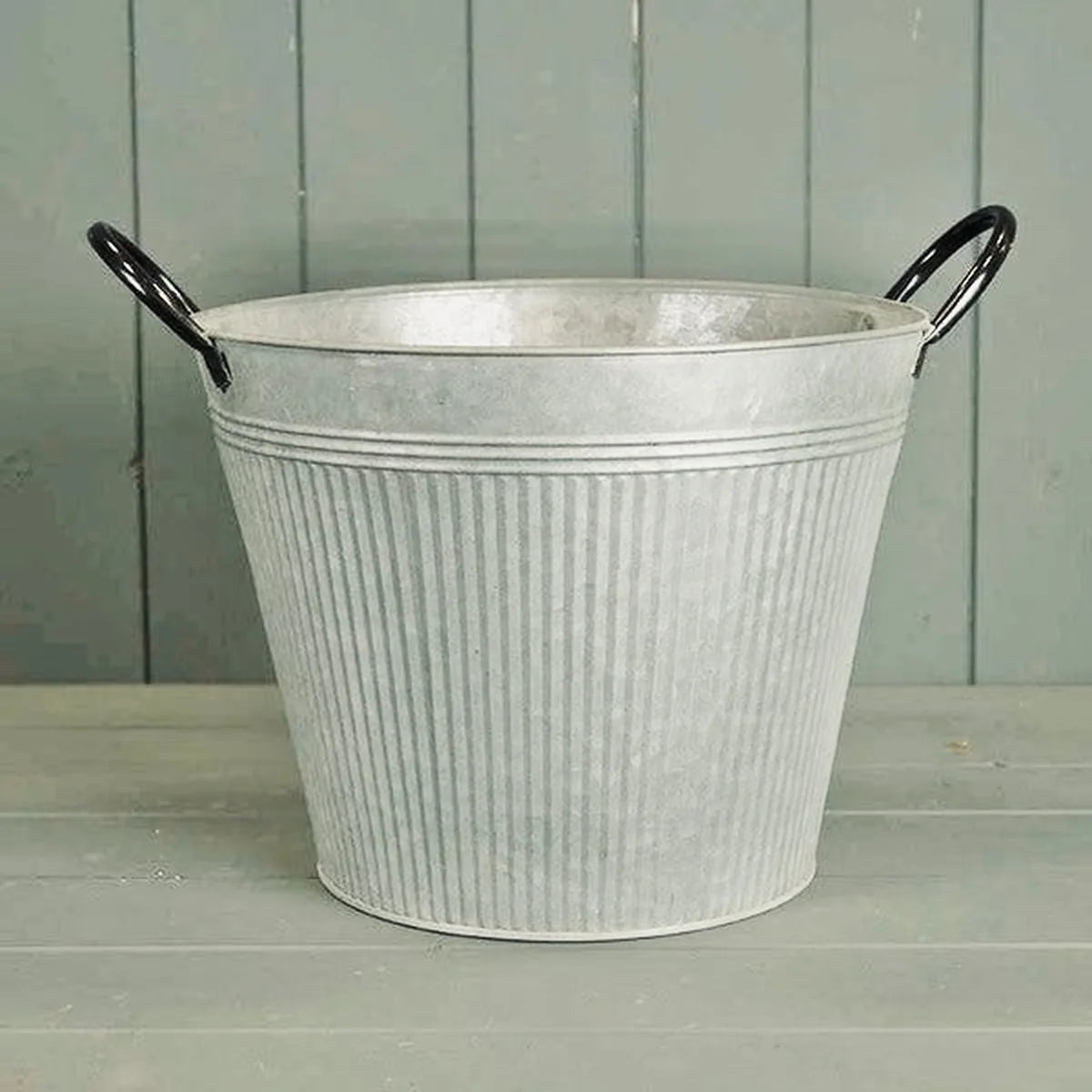 Empty round ribbed aged zinc planter with black loop handles showing tapered metal shape and open top