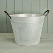 Empty round ribbed aged zinc planter with black loop handles showing tapered metal shape and open top