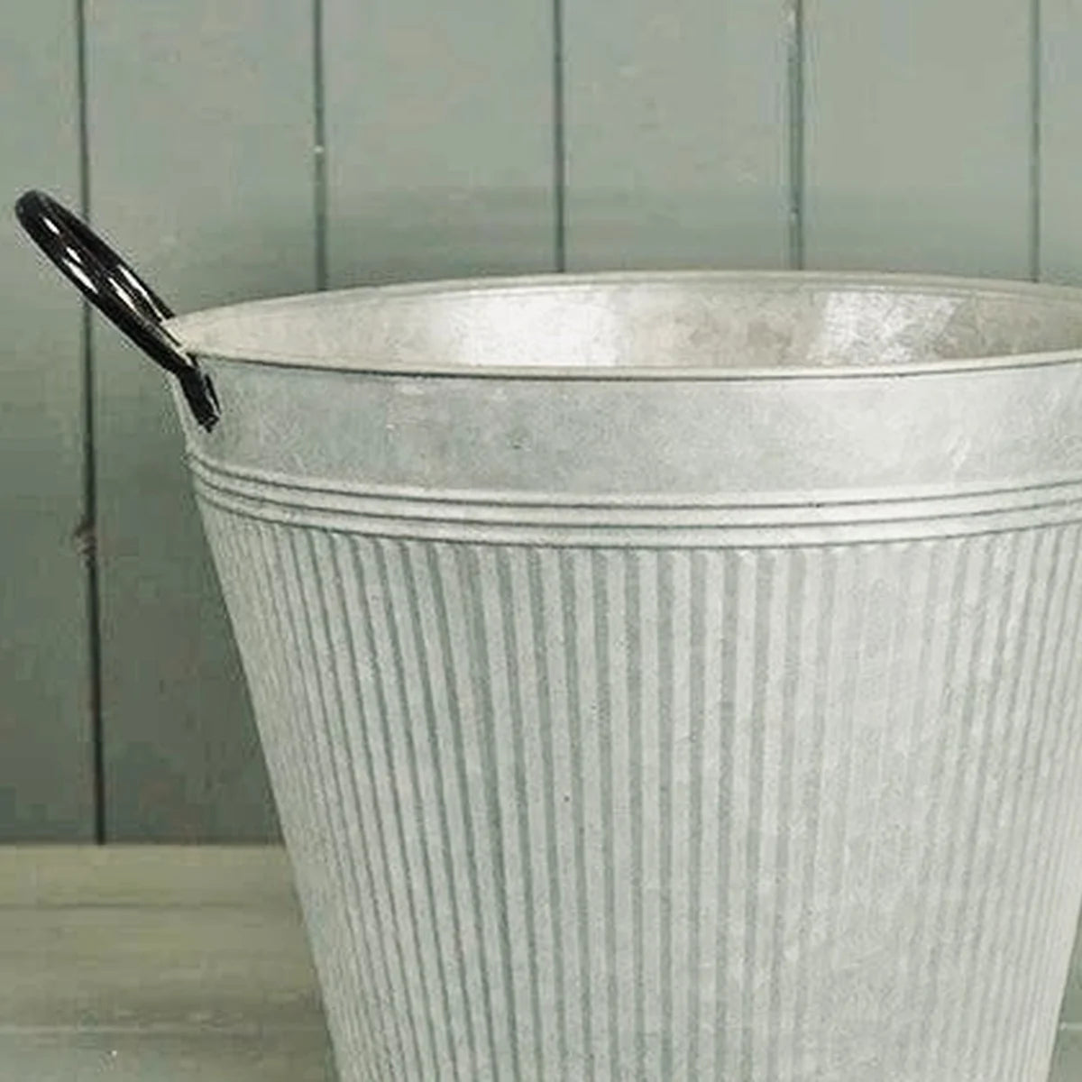 Close-up detail of aged zinc planter upper rim black handle and vertical ribbed metal finish