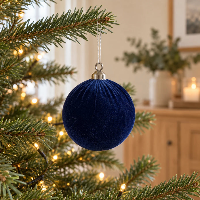 Royal blue velvet Christmas bauble from Starlight Express hanging on a decorated holiday tree.