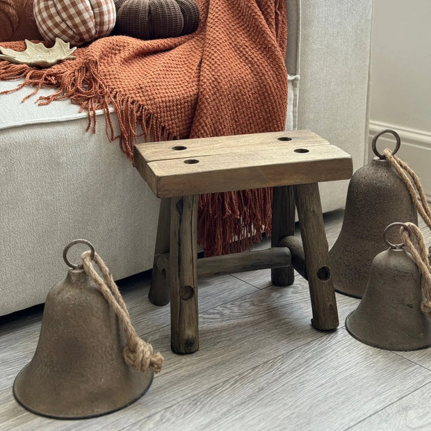 Rustic Brass Coloured Bell, large rustic bells beside a wooden stool and orange throw