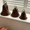 Rustic Brass Coloured Bell, three brown bells in graduated sizes beside window shutters