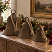 Rustic brass-coloured decorative bells in three sizes styled with evergreen garland and burgundy ribbon on an oak console