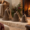 Large medium and small rustic brass-coloured bells arranged beside a country stone fireplace