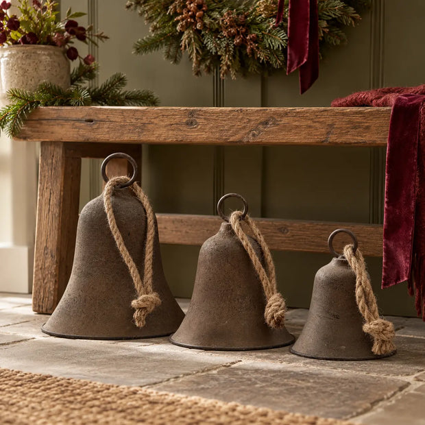 Three graduated rustic brass-coloured bells with jute rope styled beneath an oak hallway bench