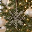 Rustic metal gem snowflake decoration hanging on a Christmas tree with neutral baubles.