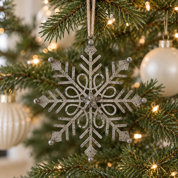 Rustic metal gem snowflake decoration hanging on a Christmas tree with neutral baubles.