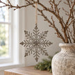 Rustic hanging snowflake with rope loop on a twig display beside a neutral stone vase.