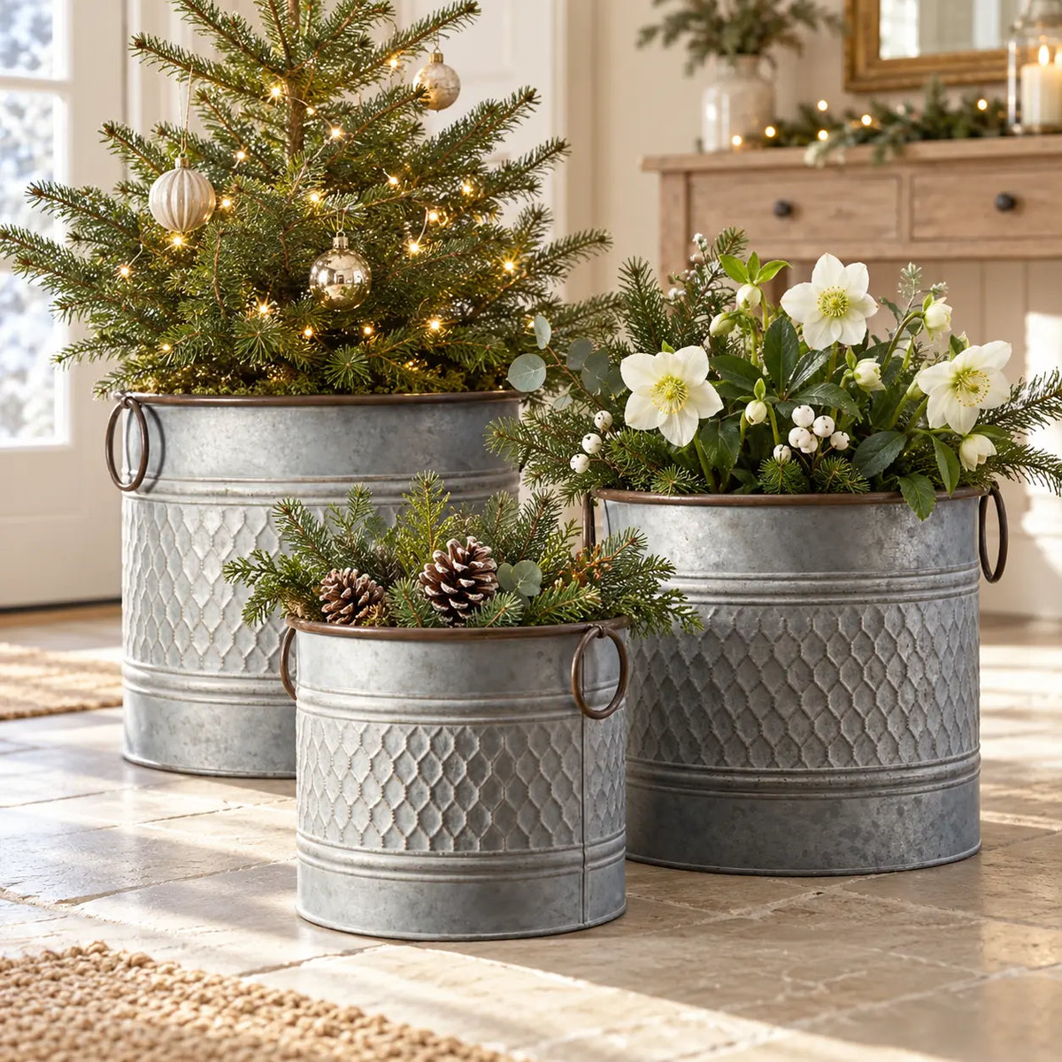 Three rustic zinc honeycomb planter pots styled with a small Christmas tree, white flowers and pinecones in a light hallway