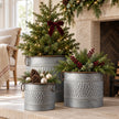 Set of three zinc honeycomb planters with Christmas greenery, berries and baubles beside a cottage fireplace