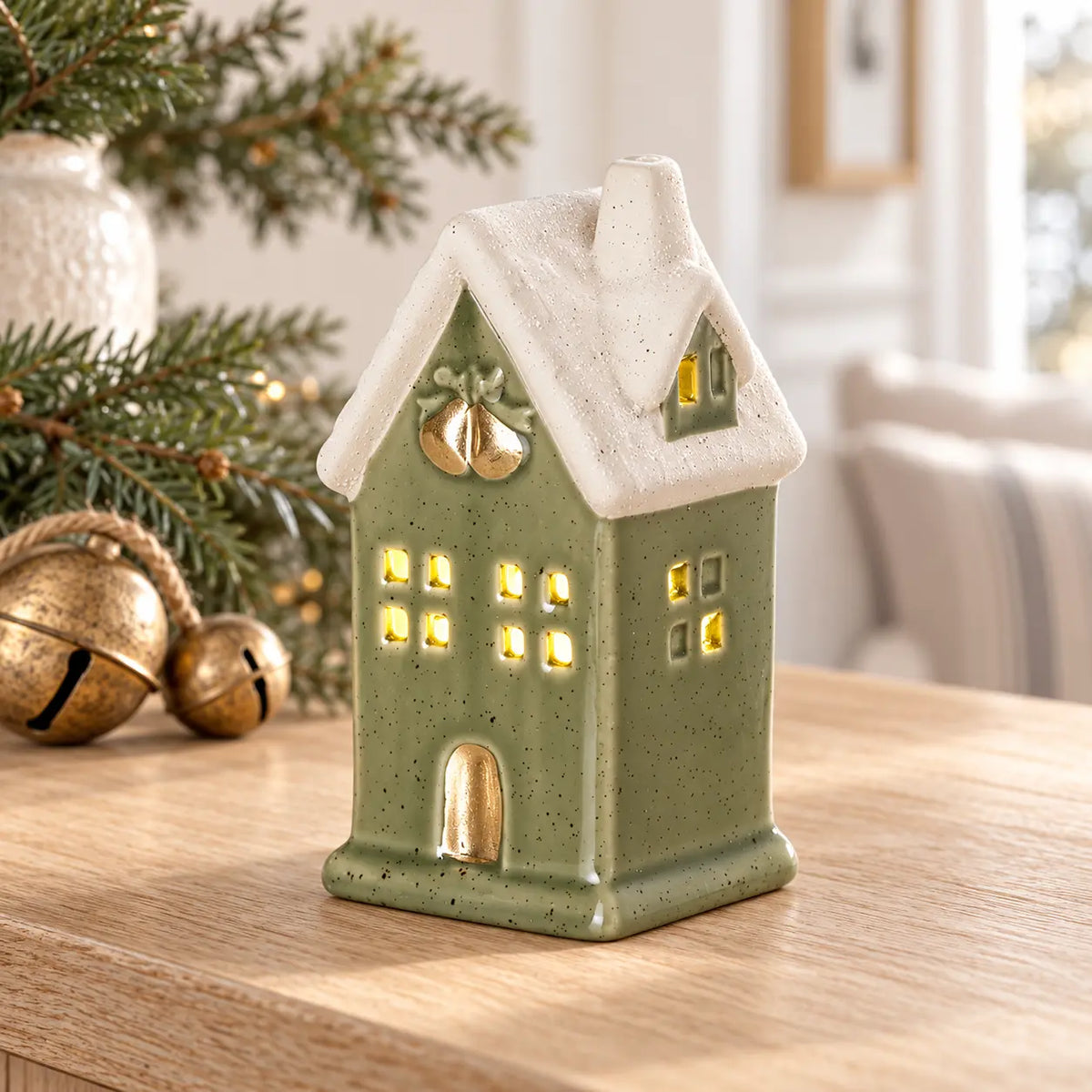 Sage green LED light up ceramic house on oak console with Christmas greenery and bells