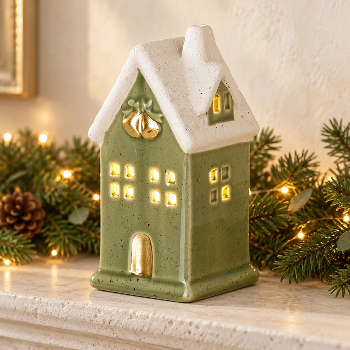 Sage green LED light up ceramic house on stone mantel with festive greenery and fairy lights