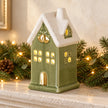 Sage green LED light up ceramic house on stone mantel with festive greenery and fairy lights