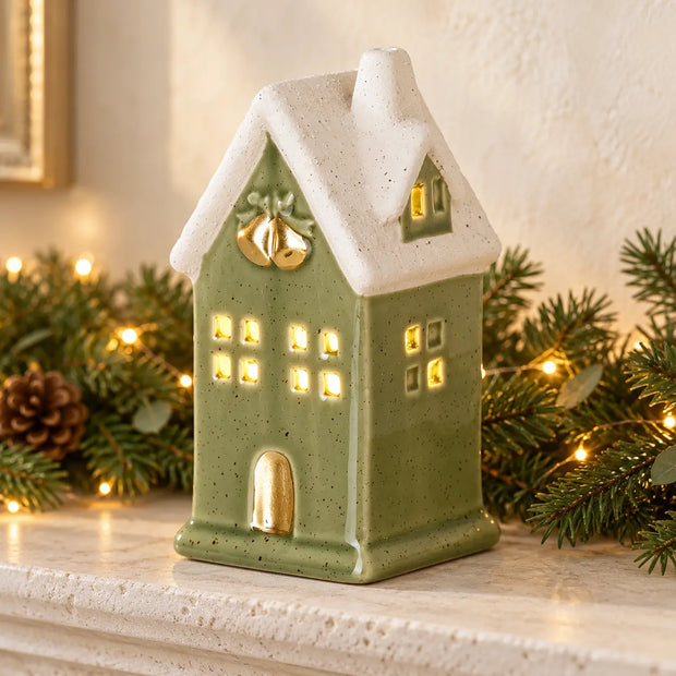 Sage green LED light up ceramic house on stone mantel with festive greenery and fairy lights