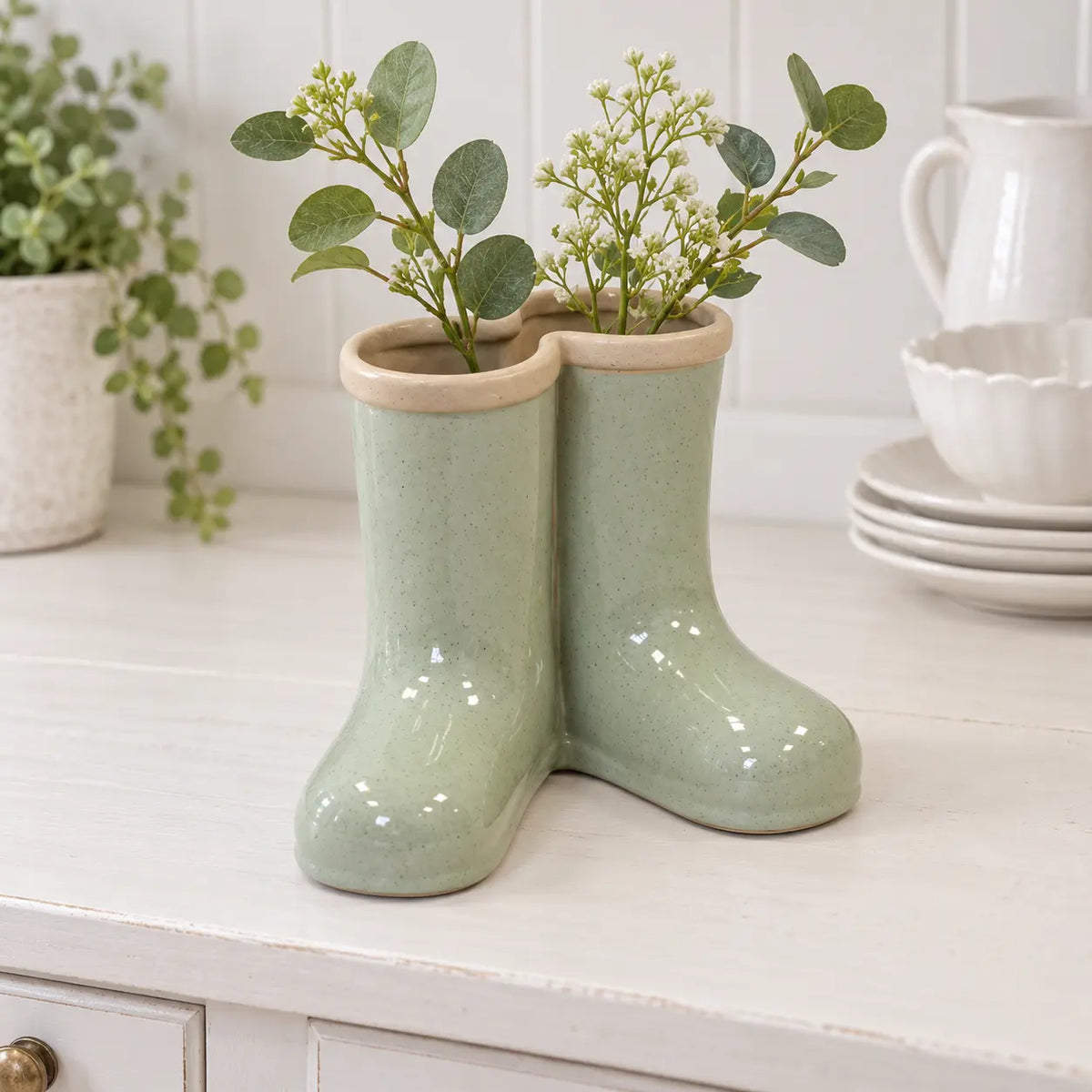 Large Satchville sage green ceramic Wellington boot vase with foliage on a dresser
