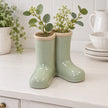 Large Satchville sage green ceramic Wellington boot vase with foliage on a dresser