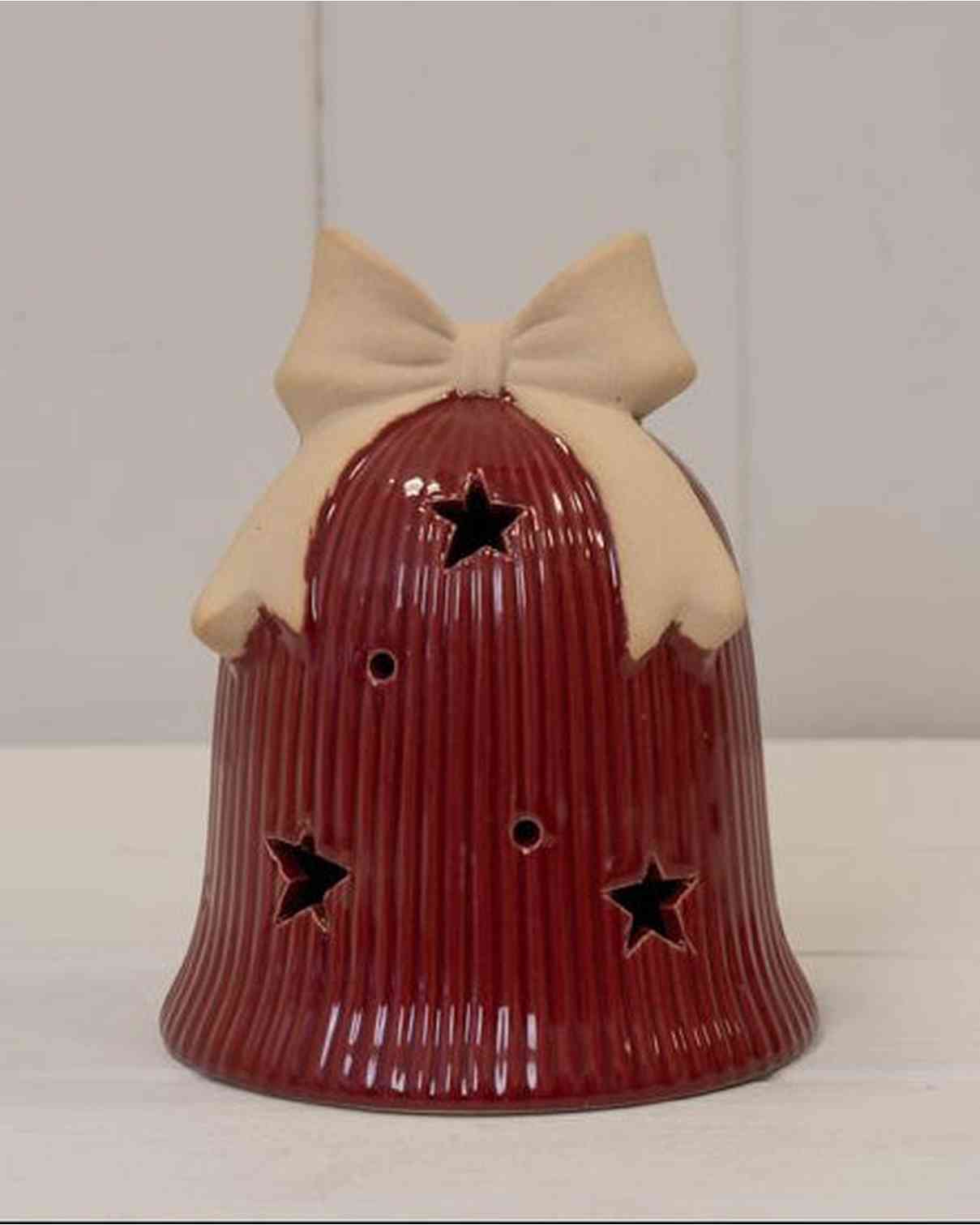 Red ceramic bell with a beige bow on a white surface and light gray background