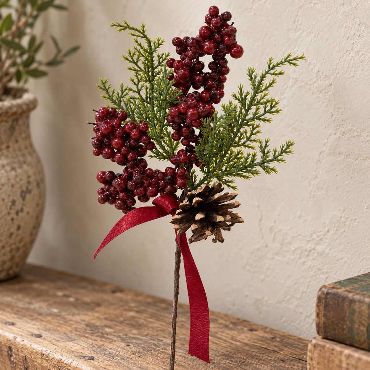 Close detail of red berries, green foliage, pinecone and red ribbon stem