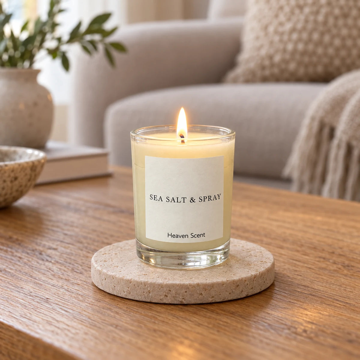 Heaven Scent Sea Salt & Spray Small Candle, lit in clear glass on a stone coaster in a living room