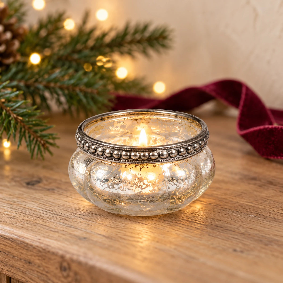 Single silver glass beaded-rim tealight holder with a lit tealight on an oak console at Christmas.