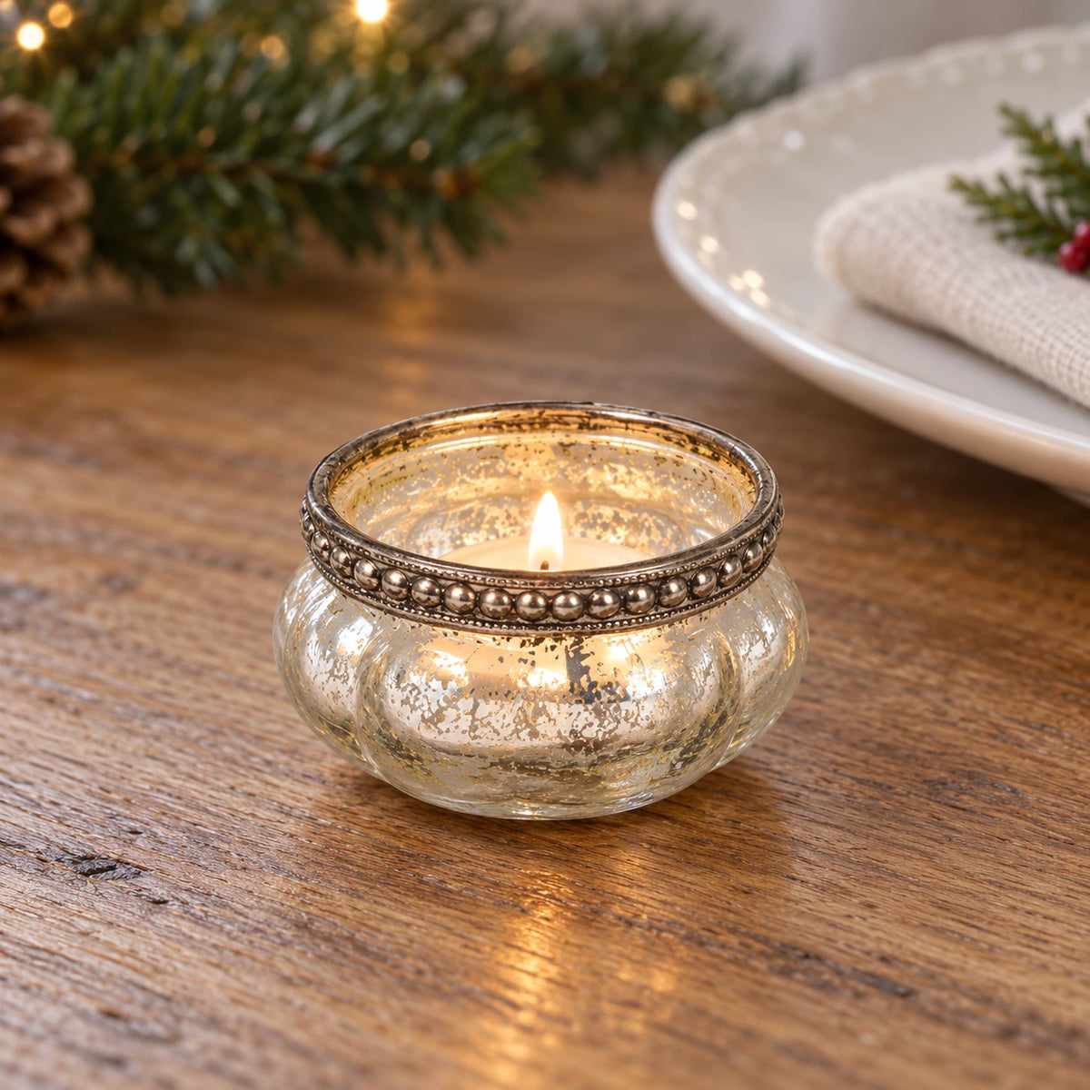 Single silver bead tealight holder with a lit tealight beside a Christmas table setting.