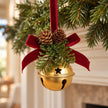 Single gold bell with burgundy bow hanging on evergreen