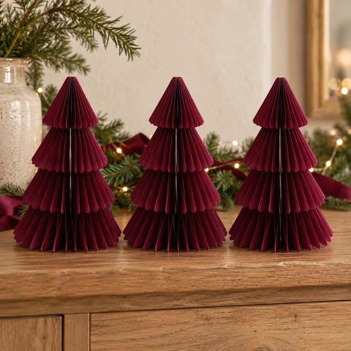 Three matching 20cm burgundy paper Christmas trees on an oak sideboard with festive greenery.