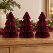 Three matching 20cm burgundy paper Christmas trees on an oak sideboard with festive greenery.