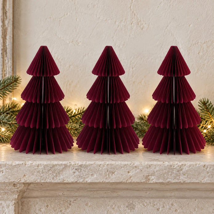 Three equal-sized burgundy paper Christmas trees side by side on a stone mantel.