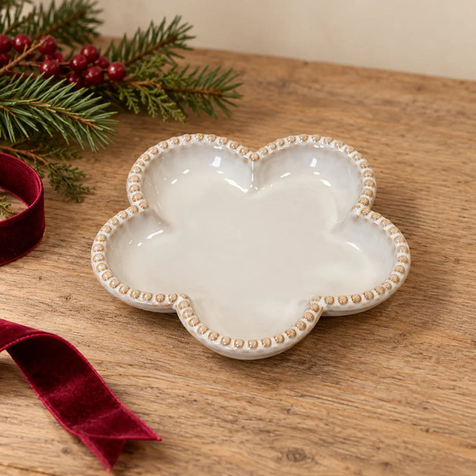 Small natural ceramic flower plate with bobble rim beside Christmas greenery and burgundy ribbon