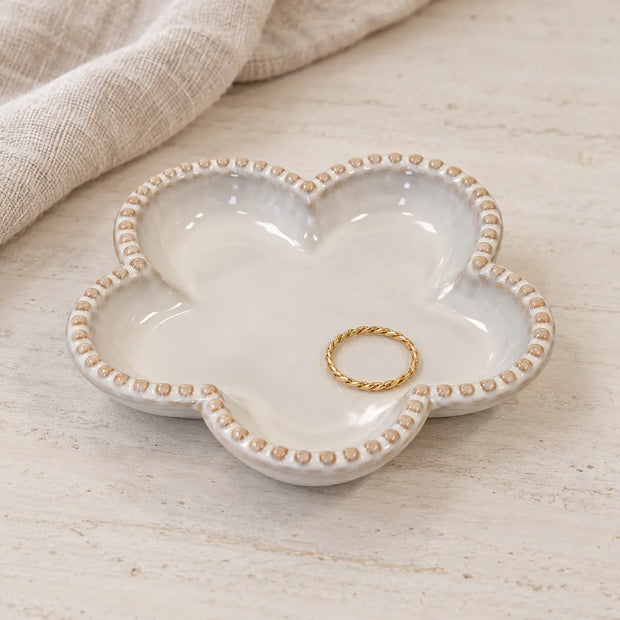 Small flower-shaped ceramic trinket plate holding a gold ring on a stone dresser