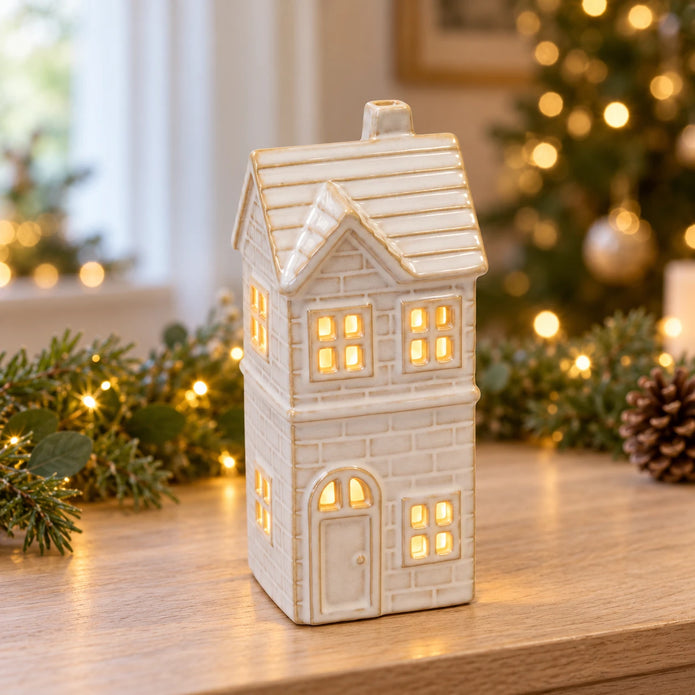 Small ivory glazed ceramic LED house glowing on an oak console with Christmas greenery