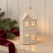 Small glazed ceramic LED house lit on a shelf with fir and burgundy ribbon