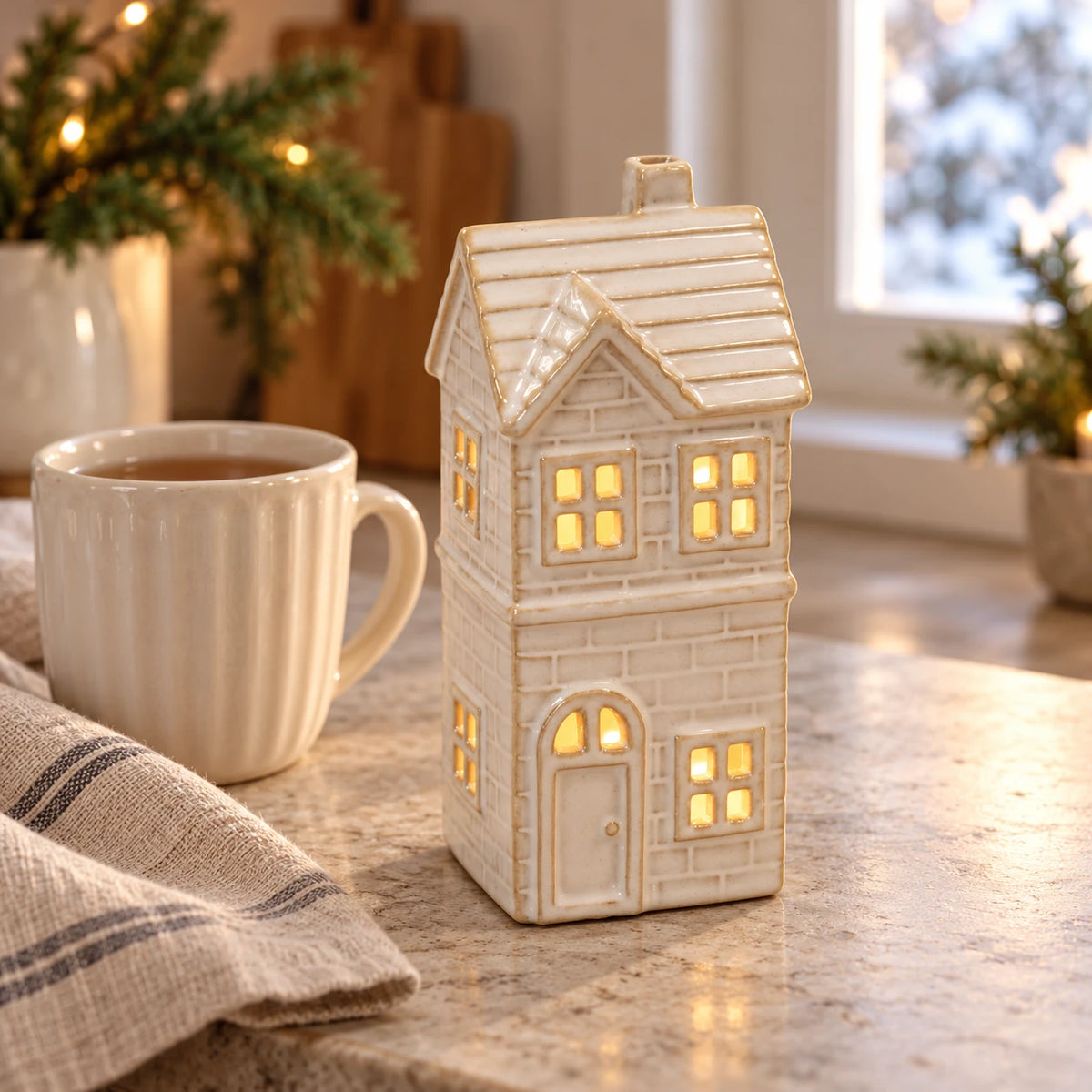 Small ceramic LED house glowing on a kitchen counter beside a mug