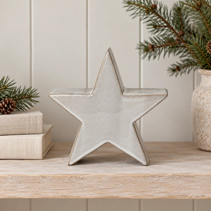 Small glazed ceramic star on shelf beside cream books and pine foliage