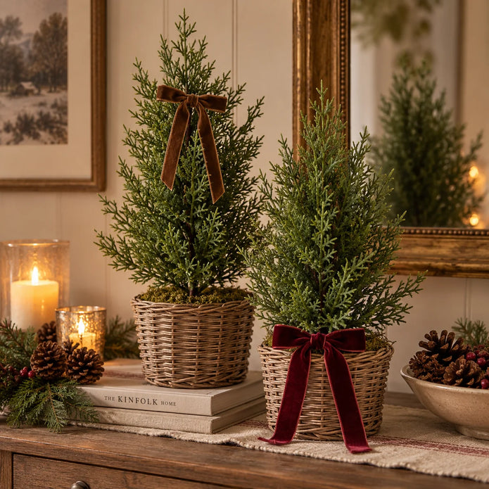 Small green fir trees with brown and burgundy velvet bows styled on a festive country-home console; baskets and bows not included