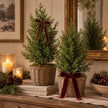 Small green fir trees with brown and burgundy velvet bows styled on a festive country-home console; baskets and bows not included