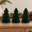 Three matching 20cm dark green paper Christmas trees on an oak sideboard with festive greenery.