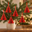Six small red paper tree decorations hanging from fir branches above an oak console.
