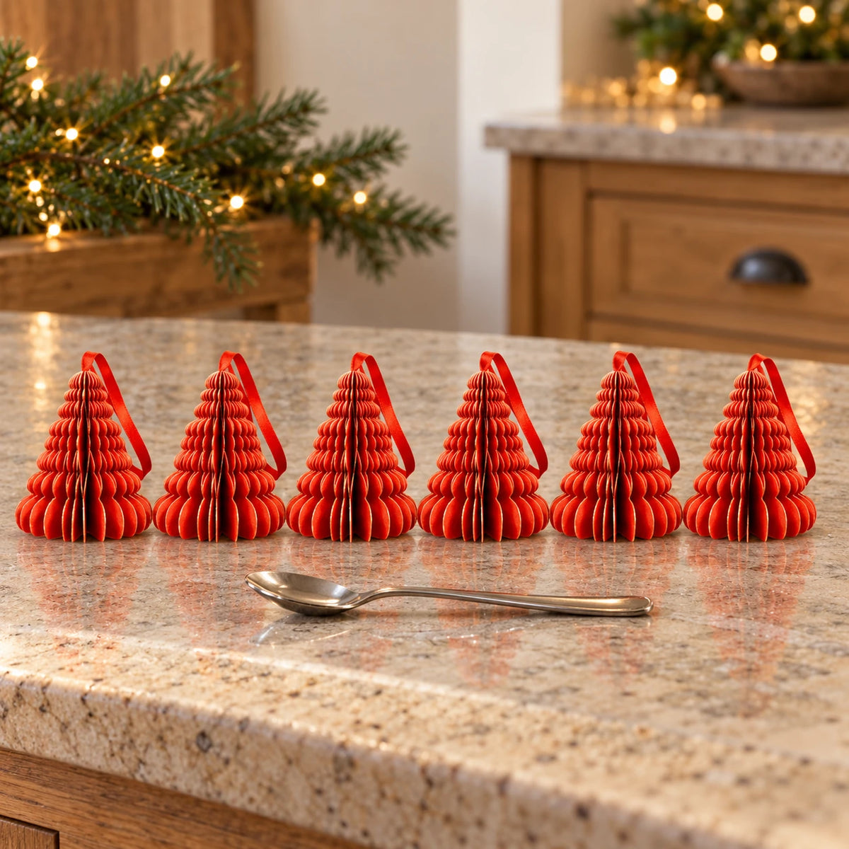 Six 9cm red paper tree ornaments on a kitchen counter beside a teaspoon.