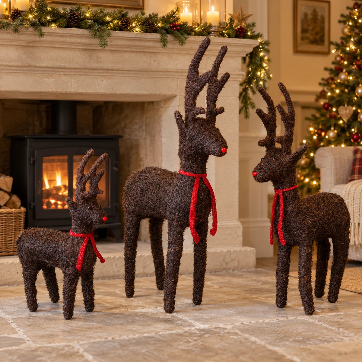 Three standing brown Salim deer with red ribbon bows beside a Christmas fireplace