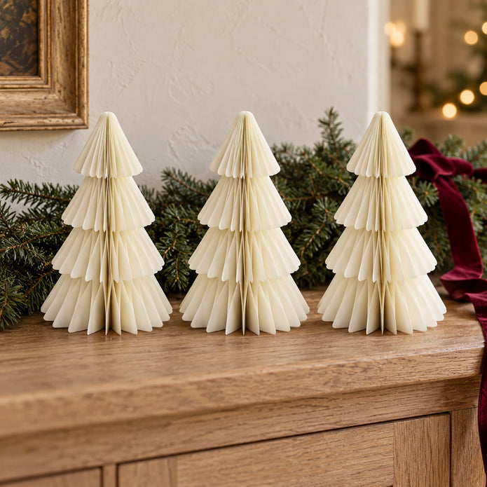 Three matching 20cm winter white paper Christmas trees on an oak sideboard with festive greenery.