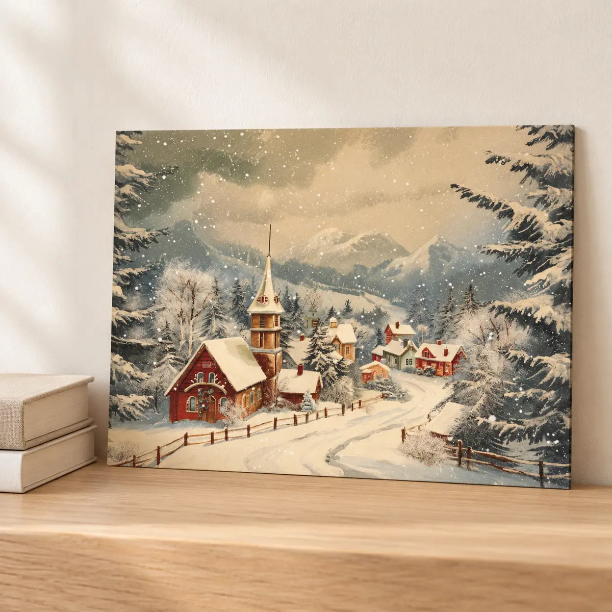 Snowy Village canvas board displayed unframed on a pale oak console beside books.