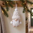 White cable-knit gonk decoration hanging from an oak peg rail with fir greenery.