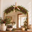 Spruce arched red berry Christmas swag with hessian bow displayed above a gold mirror