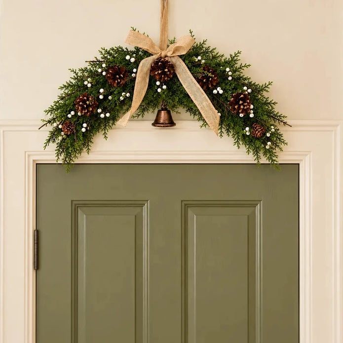 Spruce arched Christmas swag with white berries, pinecones, bells and a hessian bow centred above a sage green interior door