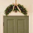 Spruce arched Christmas swag with white berries, pinecones, bells and a hessian bow centred above a sage green interior door