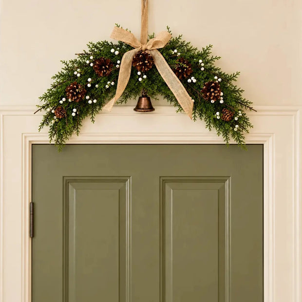 Spruce arched Christmas swag with white berries, pinecones, bells and a hessian bow centred above a sage green interior door